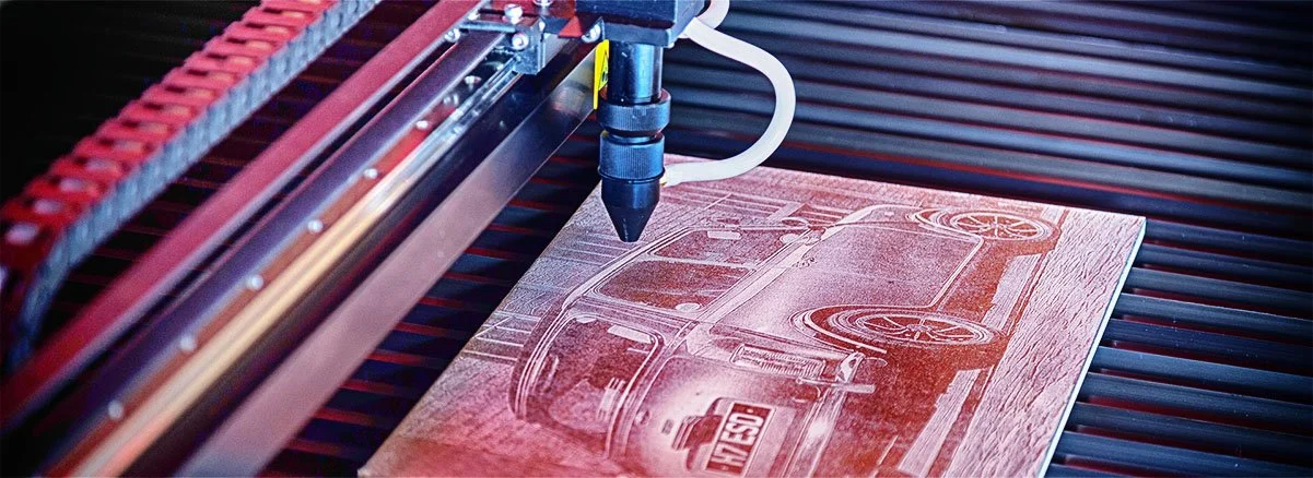 A laser engraving machine etching an image of a vintage pickup truck onto a piece of wood.