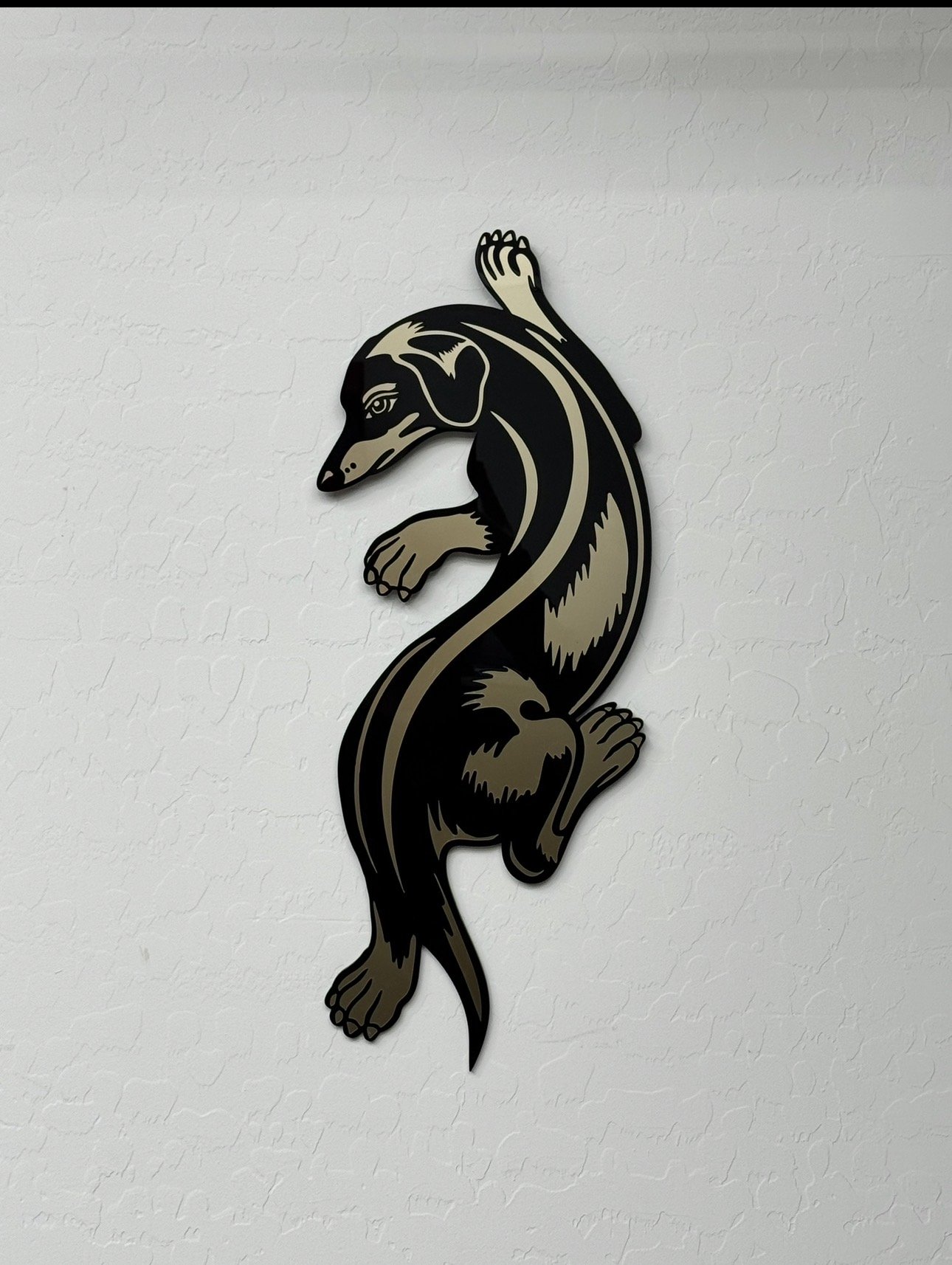 Decorative wall art of a black, tan, and beige dog silhouette with a stylized design, mounted on a white textured wall.