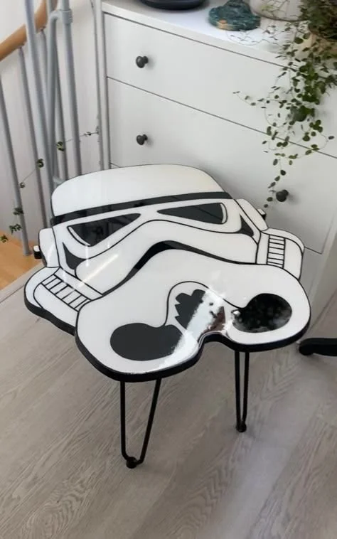 Star Wars Stormtrooper helmet-shaped table with a distressed paint finish, positioned next to a white dresser with black knobs and decorative plants.