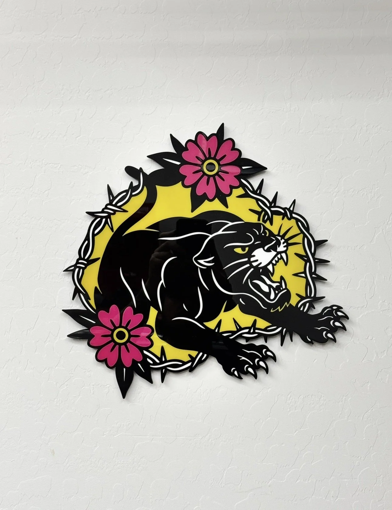Decorative wall art featuring a black panther in a crouching position, surrounded by a yellow background, barbed wire outline, and pink flowers with black leaves.