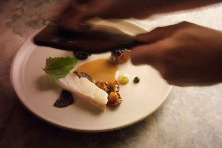 A seafood dish featuring herbs, vegetables and truffles being grated over the plate.