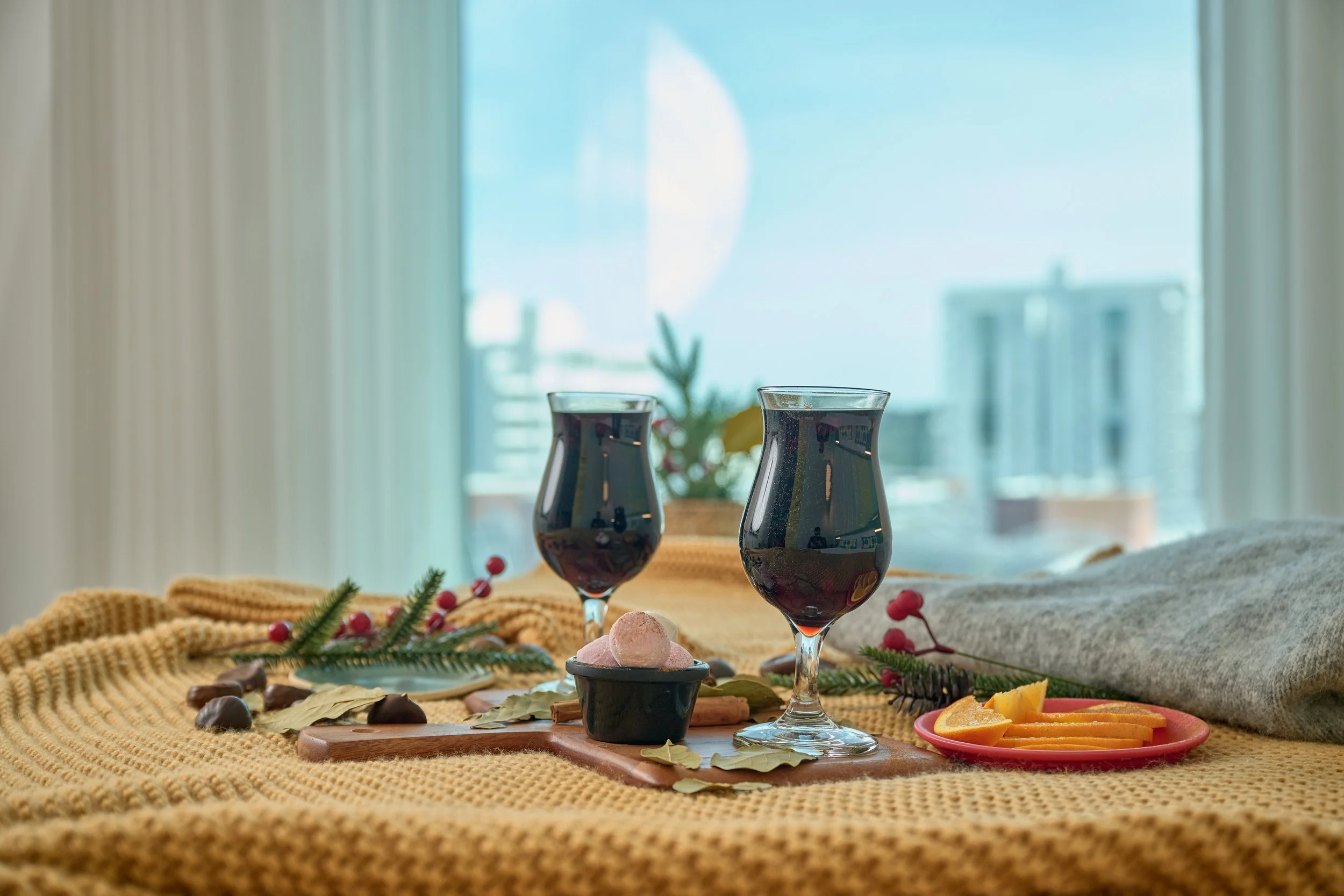 Glasses of mulled wine on a bed overlooking a window with city views