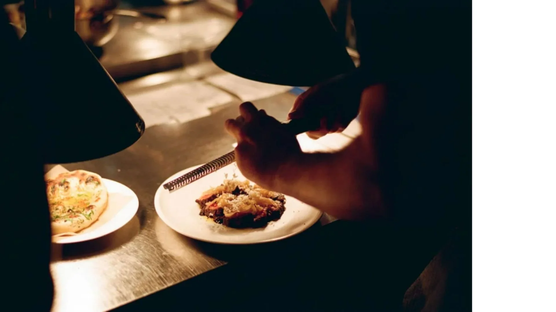 Plate of food in kitchen being grated with cheese in dark moody lighting.