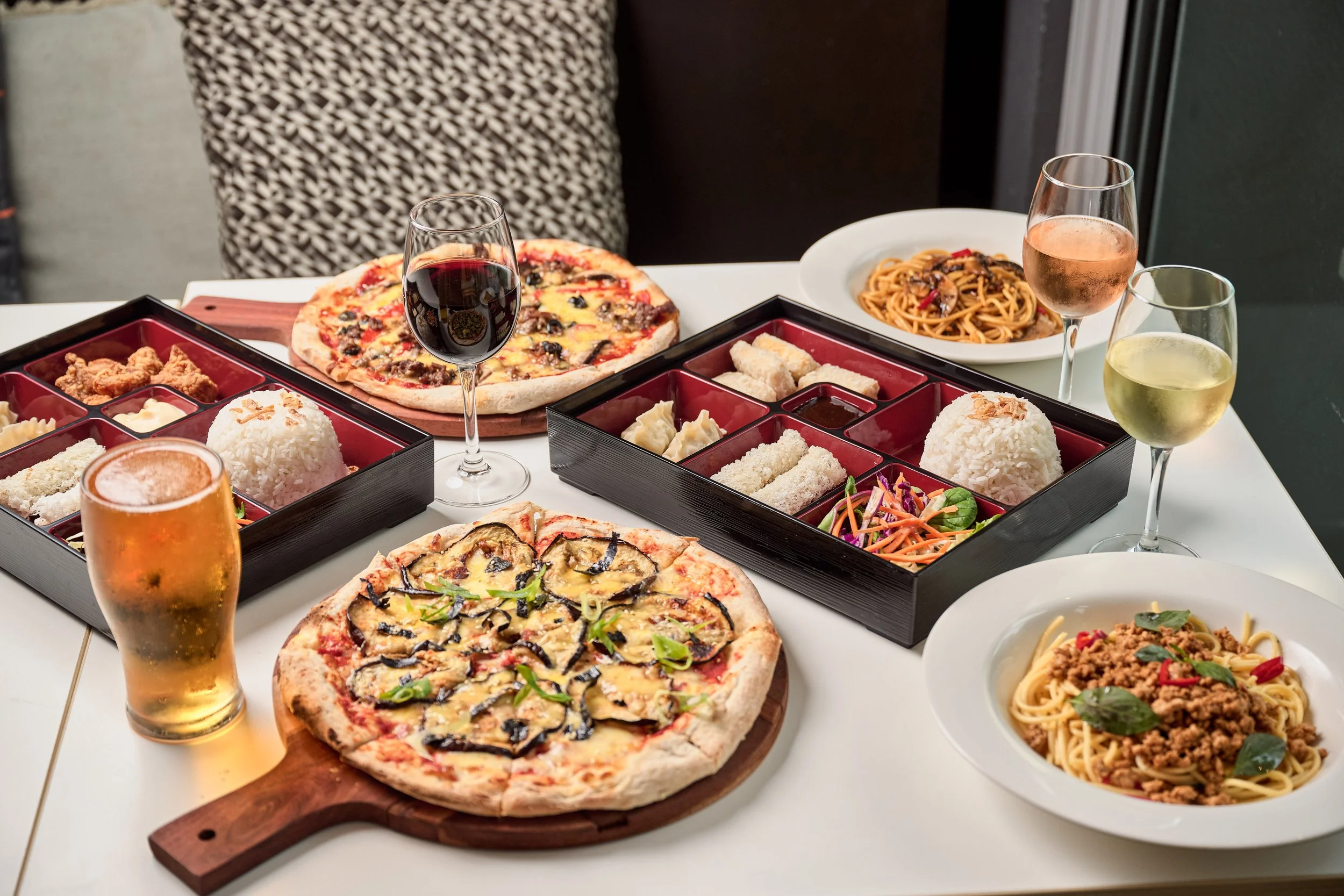 Table with pizza, beer, bento box and glasses of wine