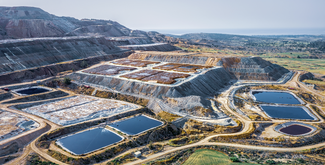 A large open-pit mining operation with terraced benches, several rectangular water ponds, and a mountainous landscape in the background | The Downing Network