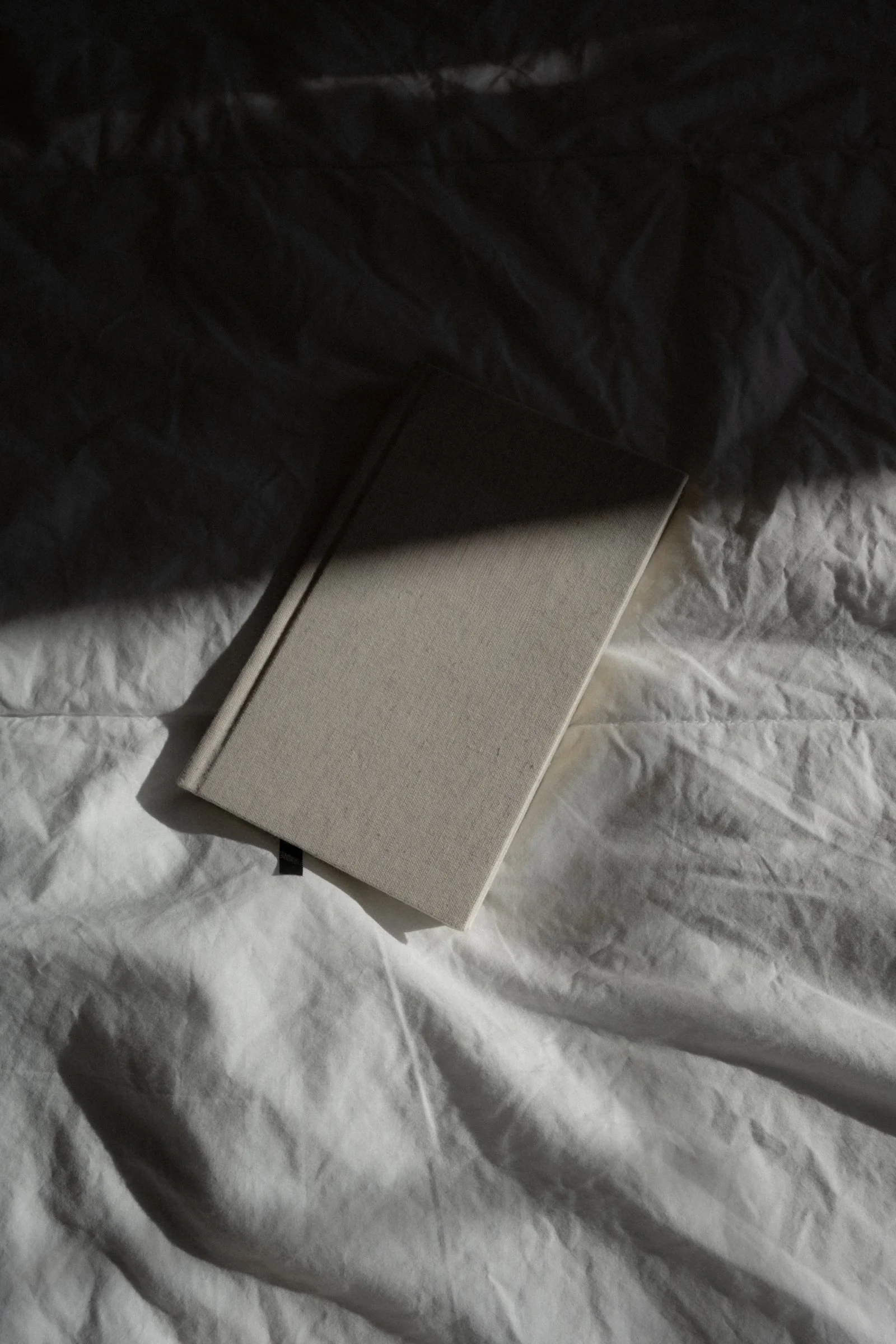 A closed beige notebook lying on crumpled white paper with a shadow cast over part of it.