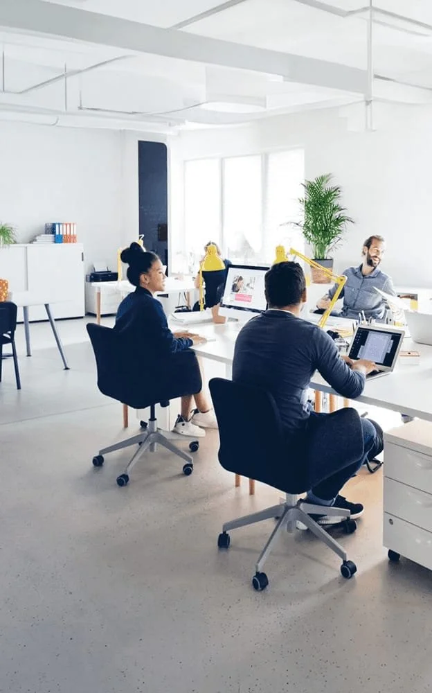 Helles, modernes Großraumbüro mit Mitarbeitern an weißen Schreibtischen.