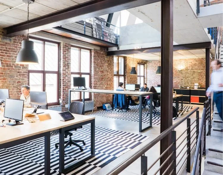 Offener Arbeitsbereich in einem modernen Büro mit großen Fenstern, Brücken und mehreren Mitarbeitern, die an Ihren Schreibtischen arbeiten.