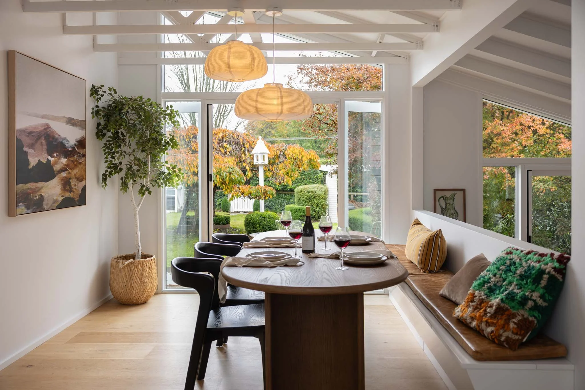 White marble kitchen island with a wooden cutting board, green persimmons, a white cloth, and a ceramic bowl with persimmons, surrounded by woven wooden chairs.