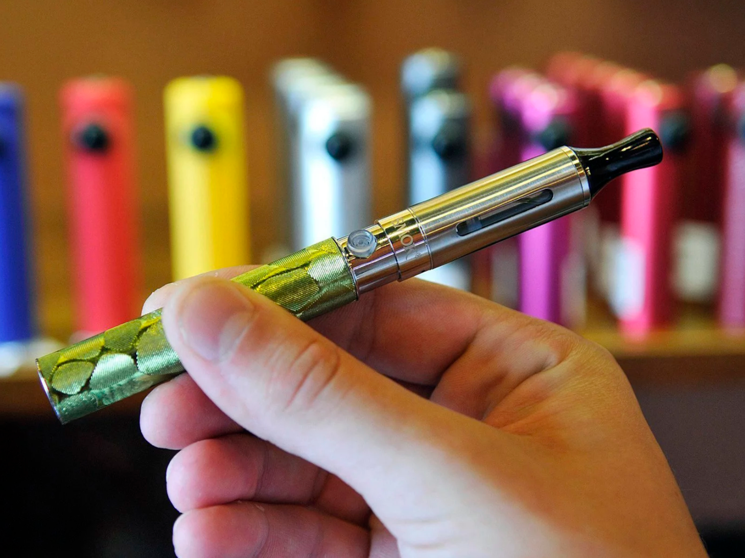 image of a hand holding a vape pen with colorful vapes in background