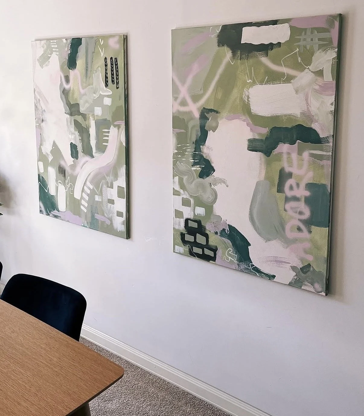 Two abstract paintings hanging on a white wall in an office or conference room. Wooden table and black chairs in the foreground.