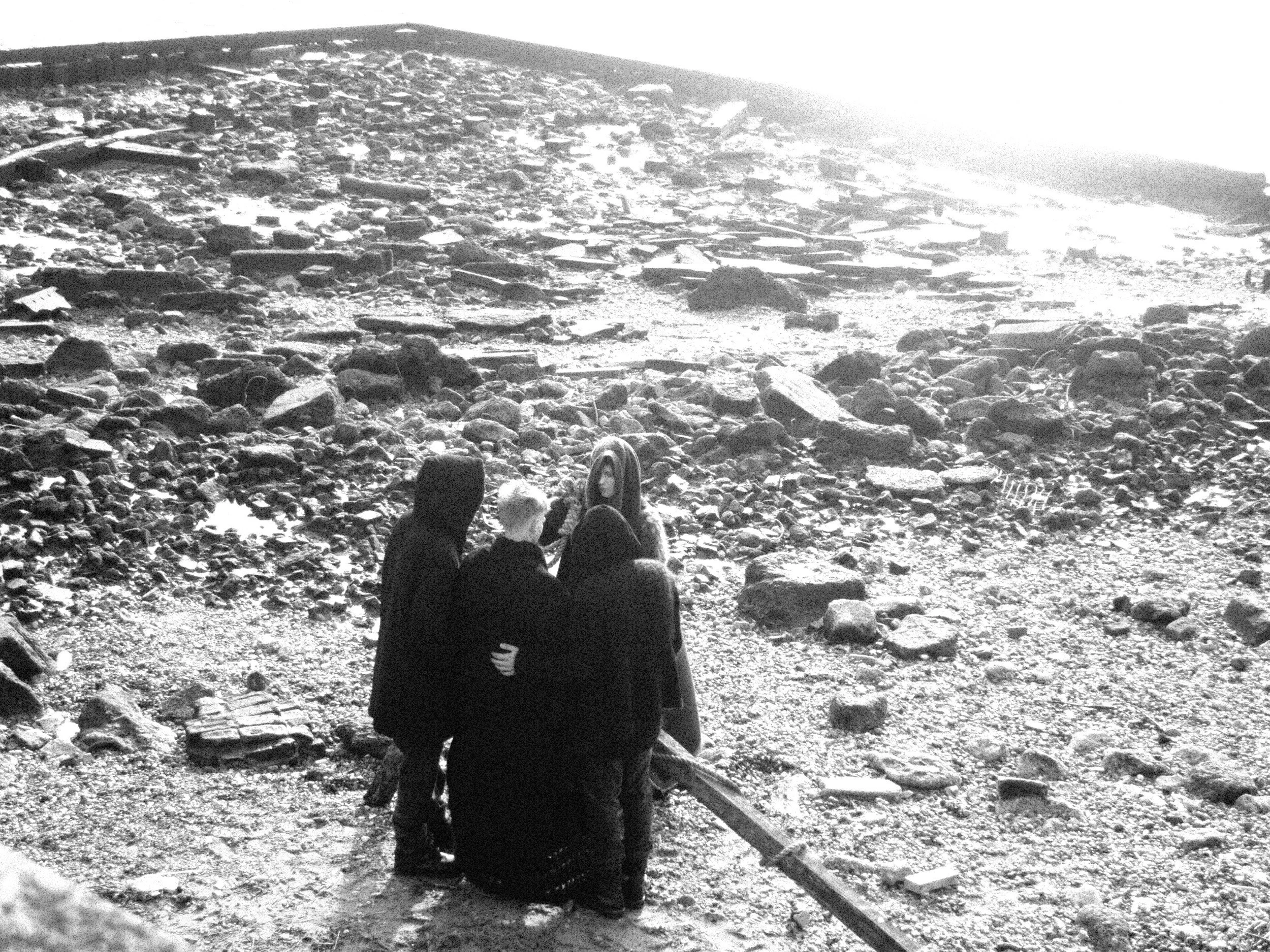 Three people sitting on a rocky beach facing the ocean at sunset or sunrise.