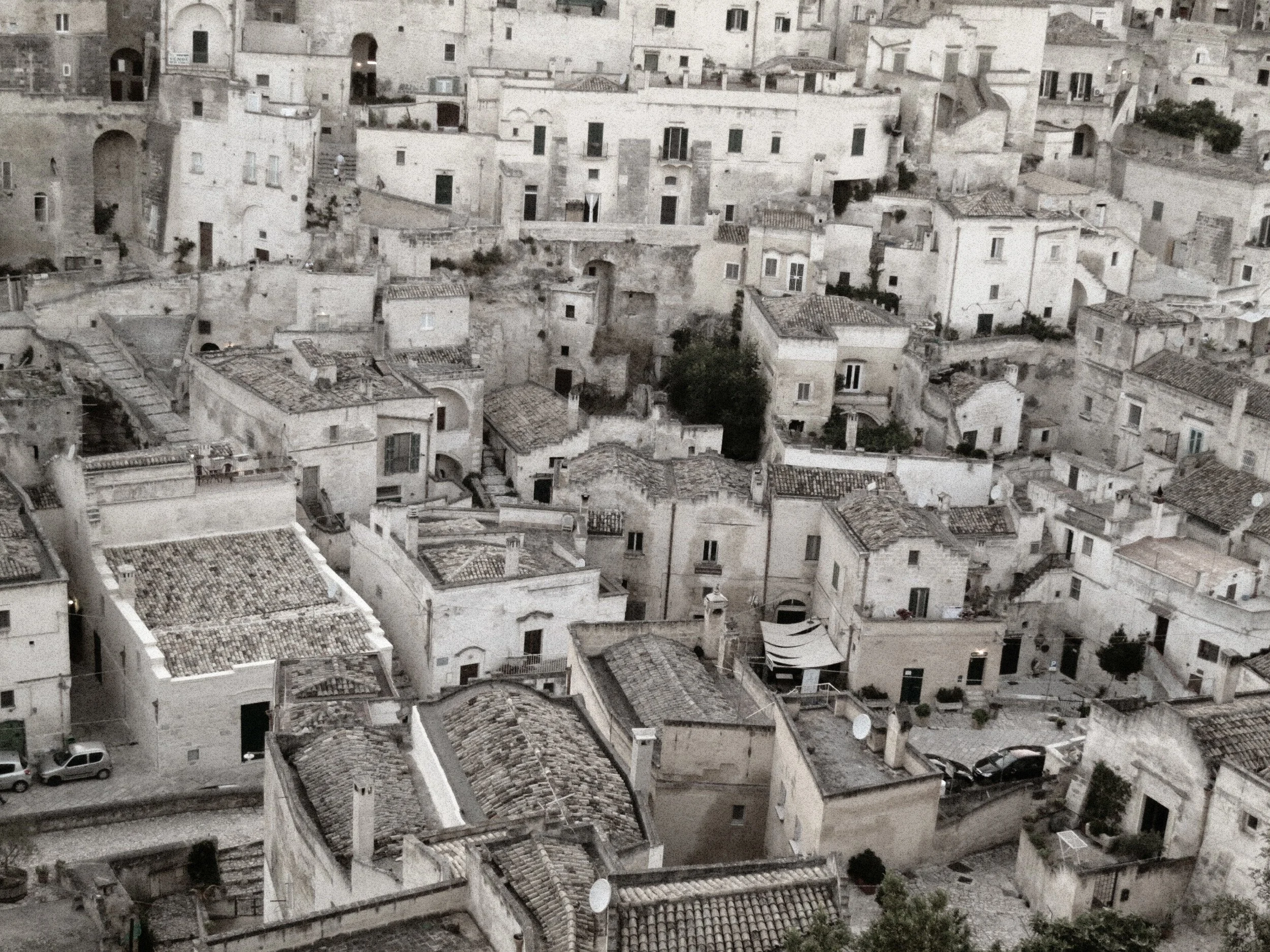 Aerial view of a densely packed hillside neighborhood featuring white stone buildings with tiled roofs and small windows.