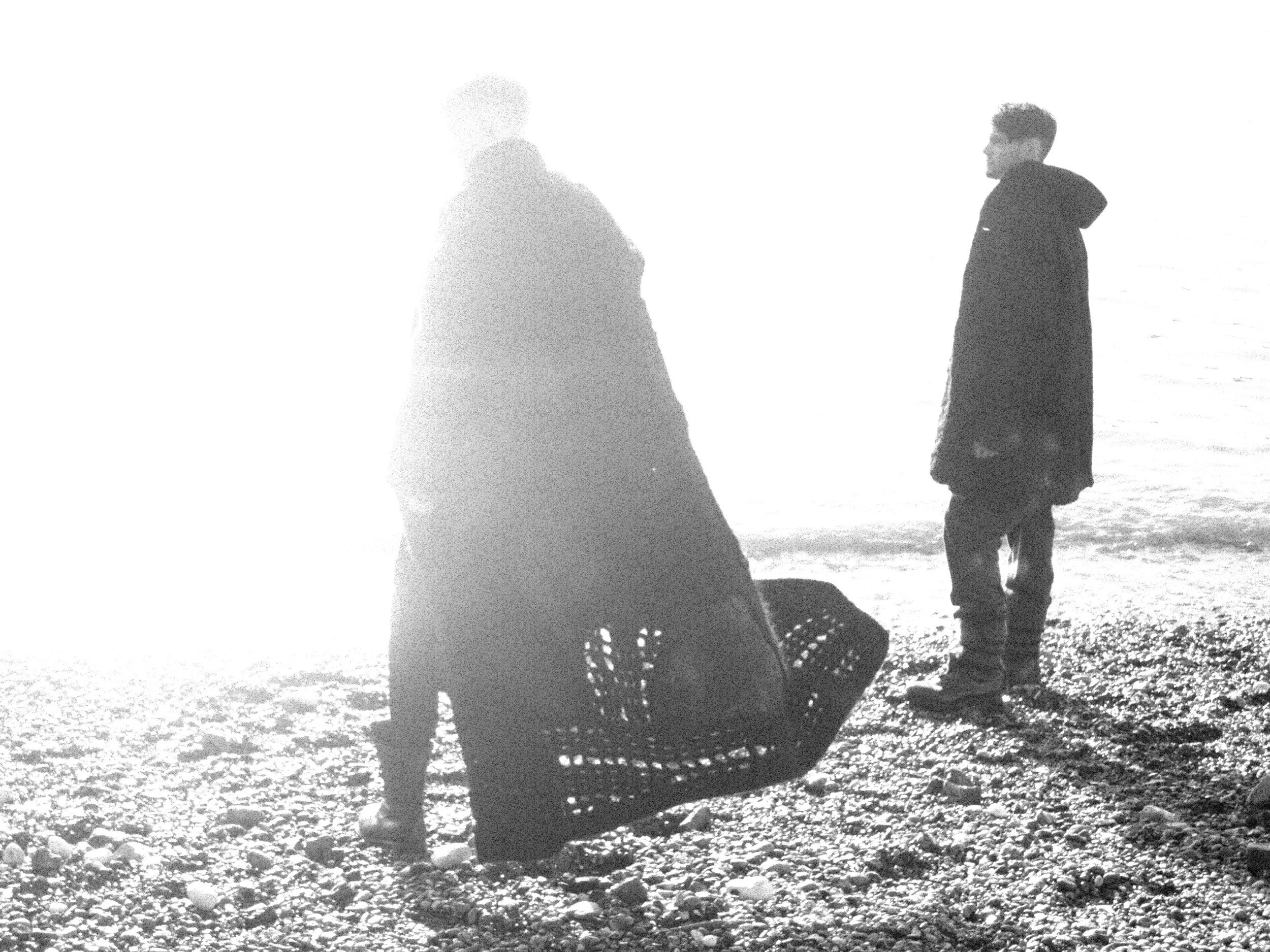 Silhouettes of a person walking on the beach near two children, with the ocean in the background.