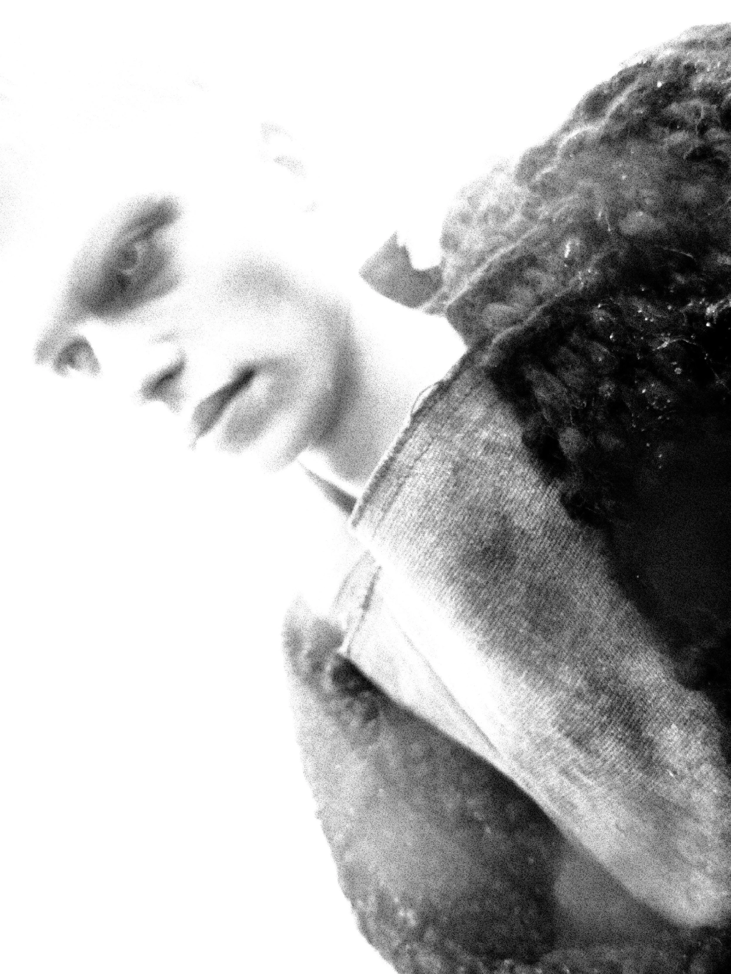 Close-up black and white photo of a person's face, showing one eye and part of the nose and lips, with textured clothing visible.