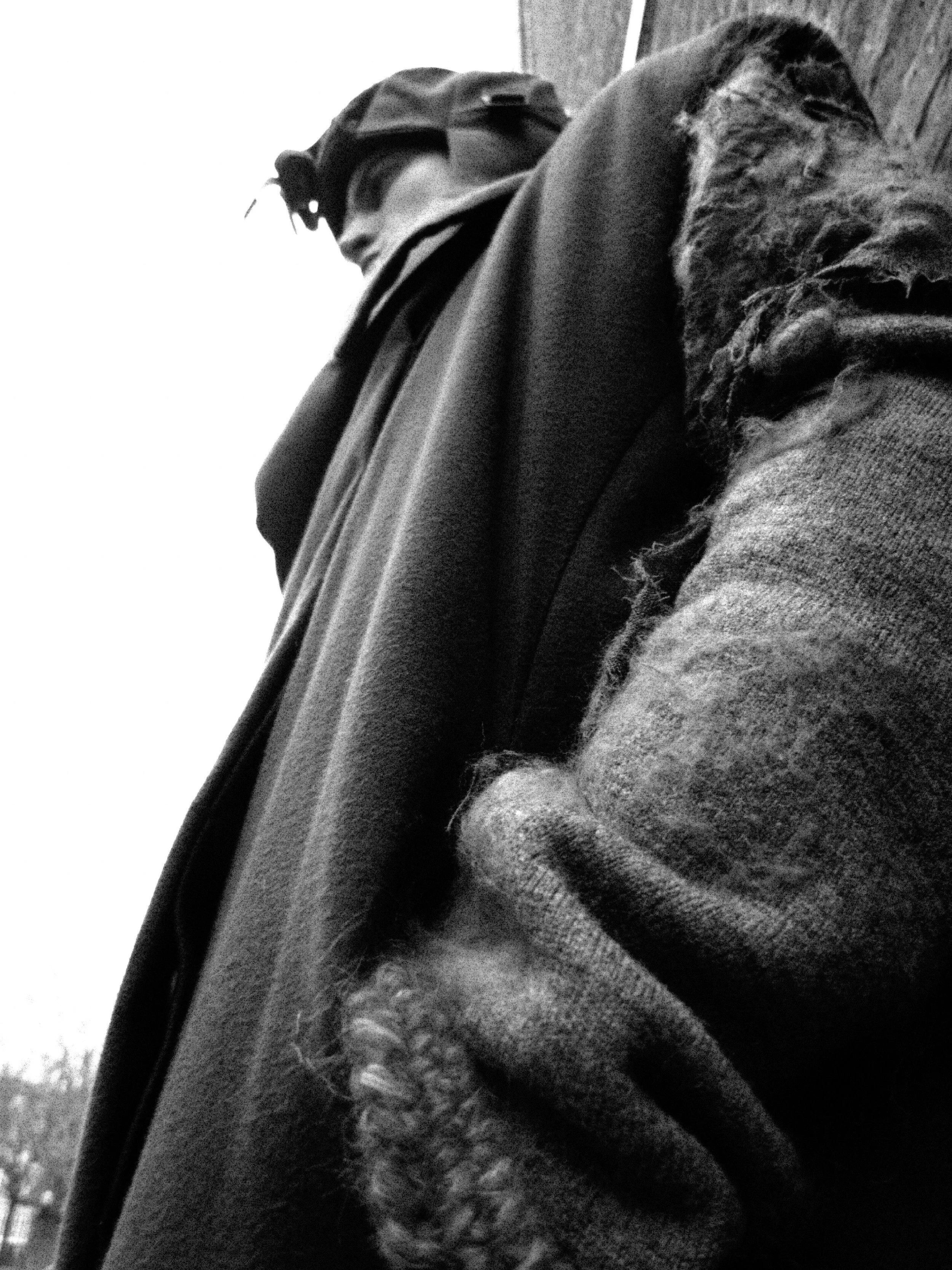 Close-up of a person wearing a hoodie and a face mask, with a textured fabric and outdoor background.