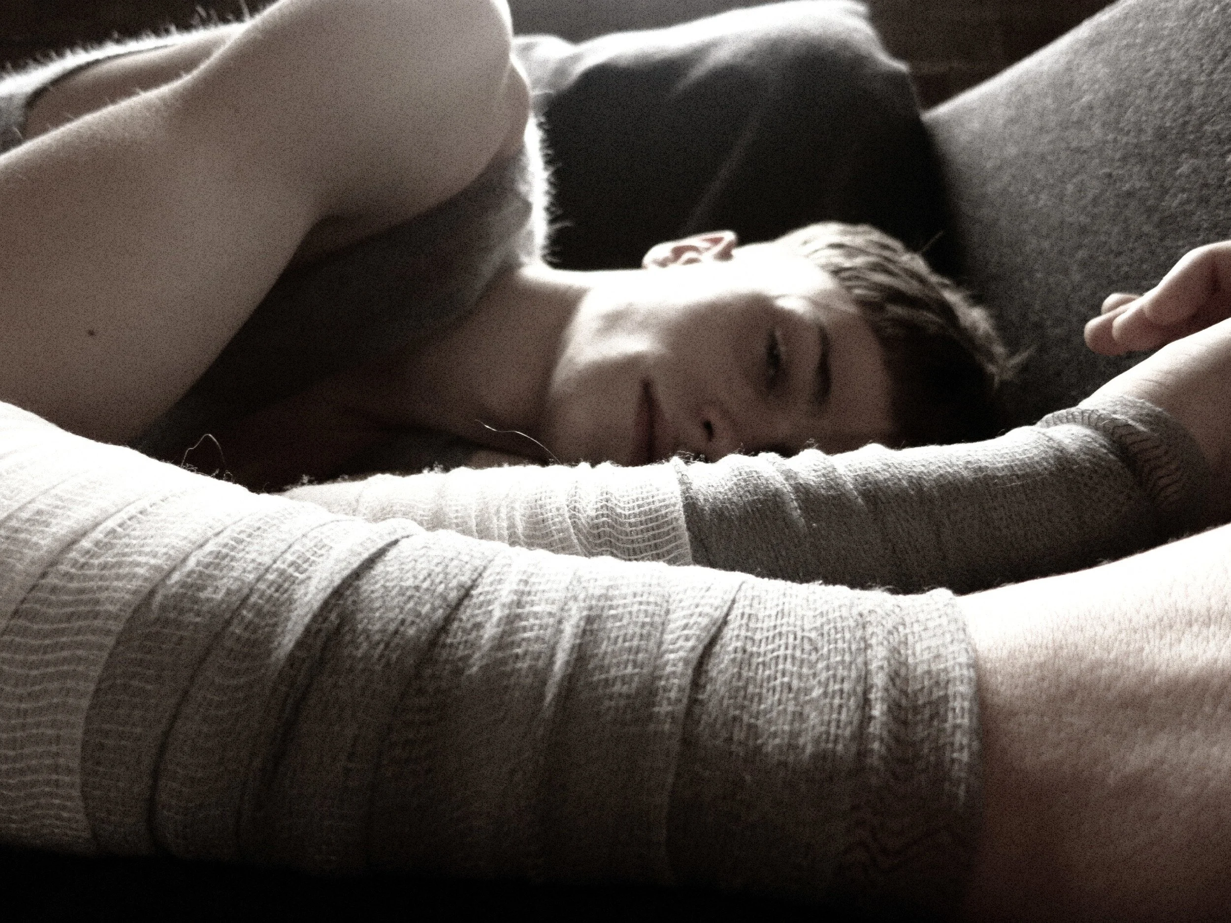 Person lying on their side with eyes closed, peacefully sleeping or resting, wearing a striped long-sleeve shirt, with a dog sleeping beside them.