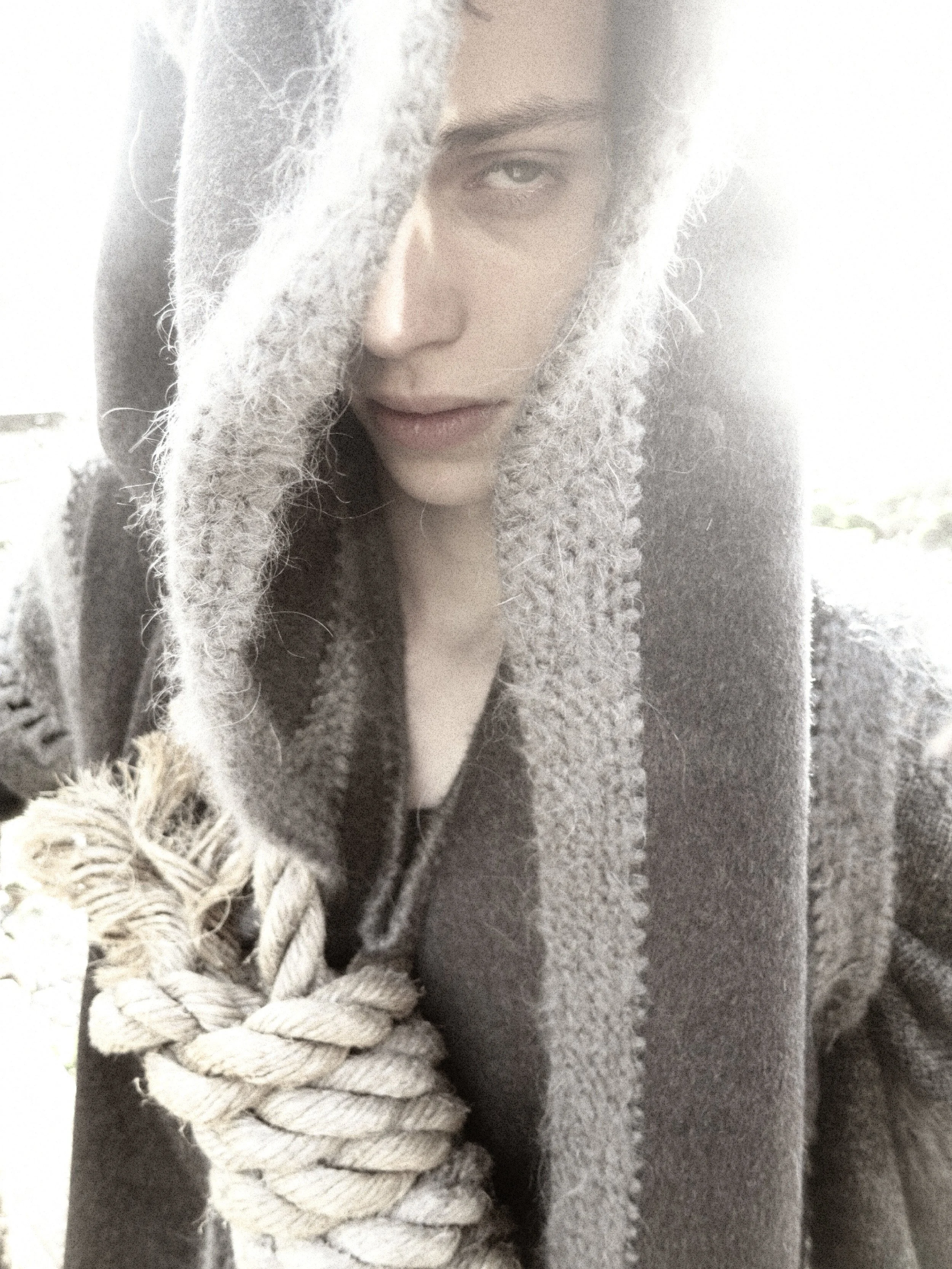 A person wearing a heavy, textured knit hooded scarf with a braid, covering part of their face and shoulder.