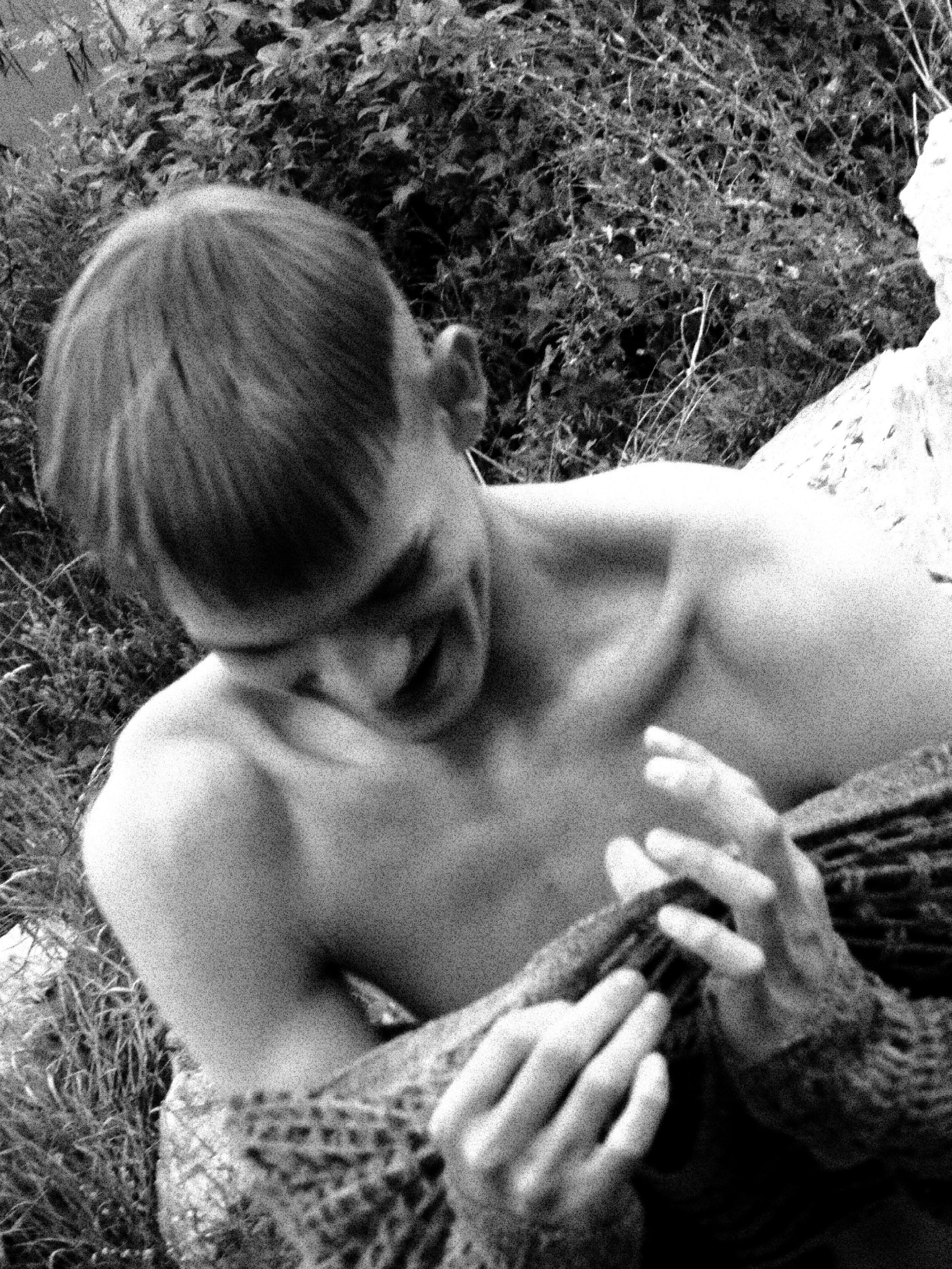 A young child with short hair leaning over a rough concrete surface, with grass and foliage in the background.