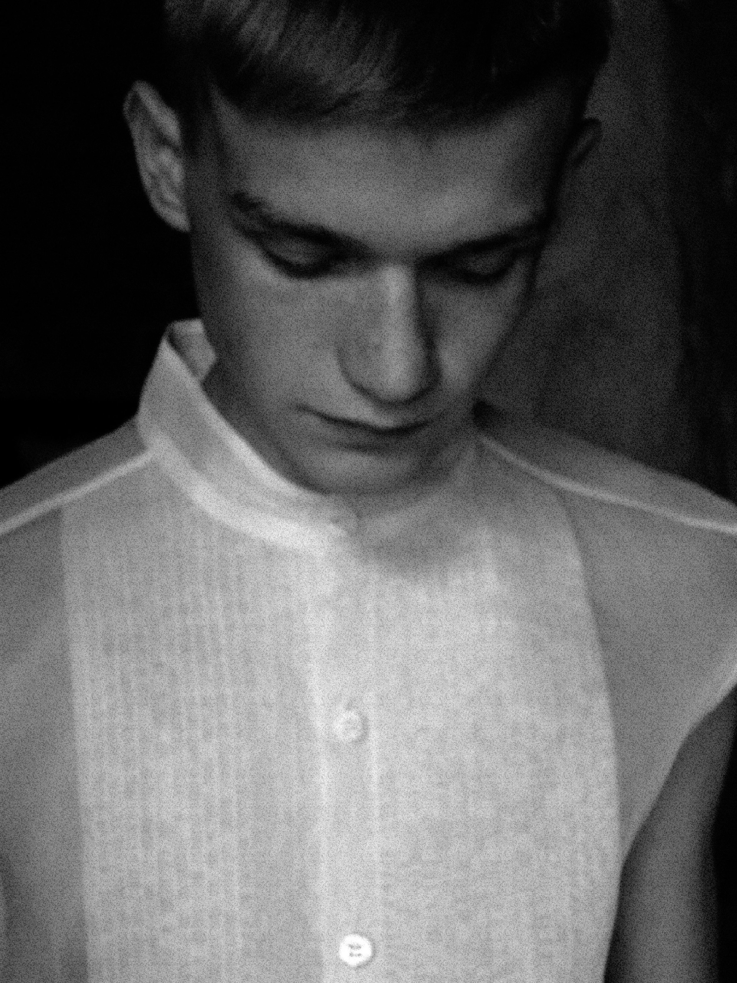 Close-up black-and-white photo of a young man's face looking down, with short hair and a calm expression.