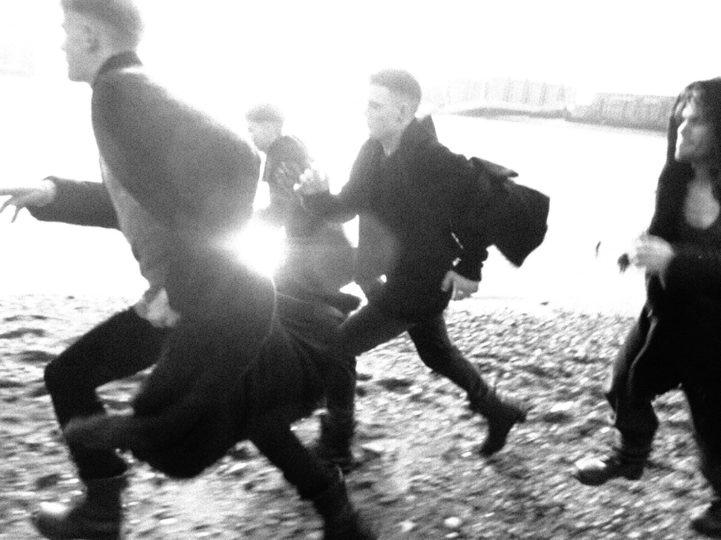 A black and white image of children playing on a sandy beach, some running and some standing, with bright sunlight creating high contrast shadows.