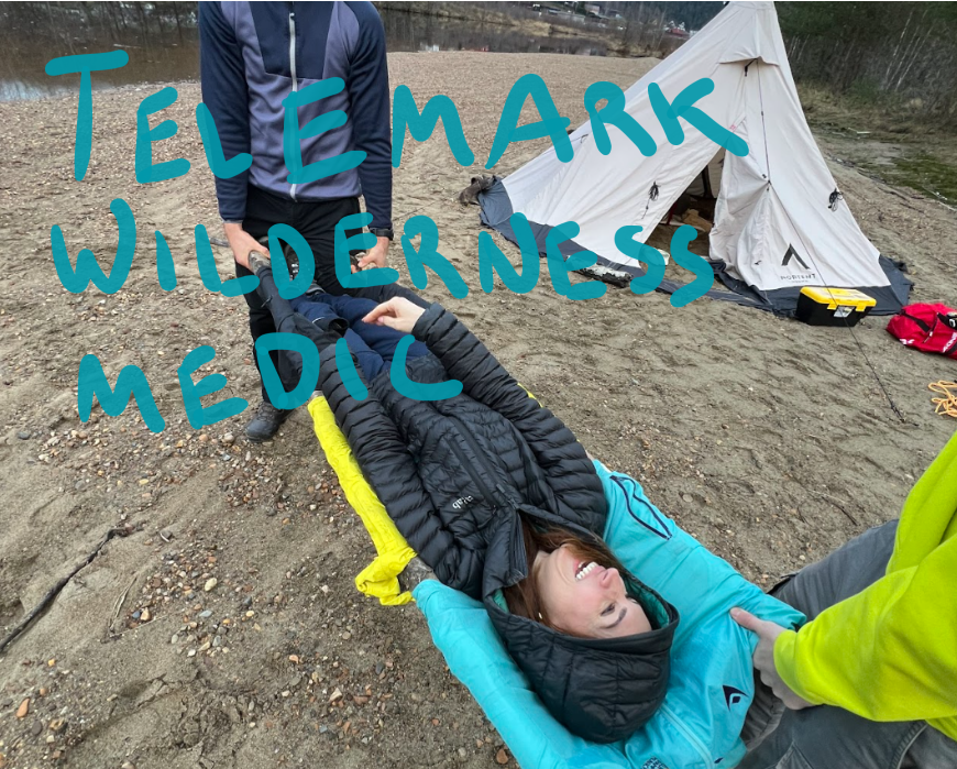 A woman lying on an improvised stretcher, being helped by two participants at the outdoor Telemark Wilderness Medic tent-classroom.