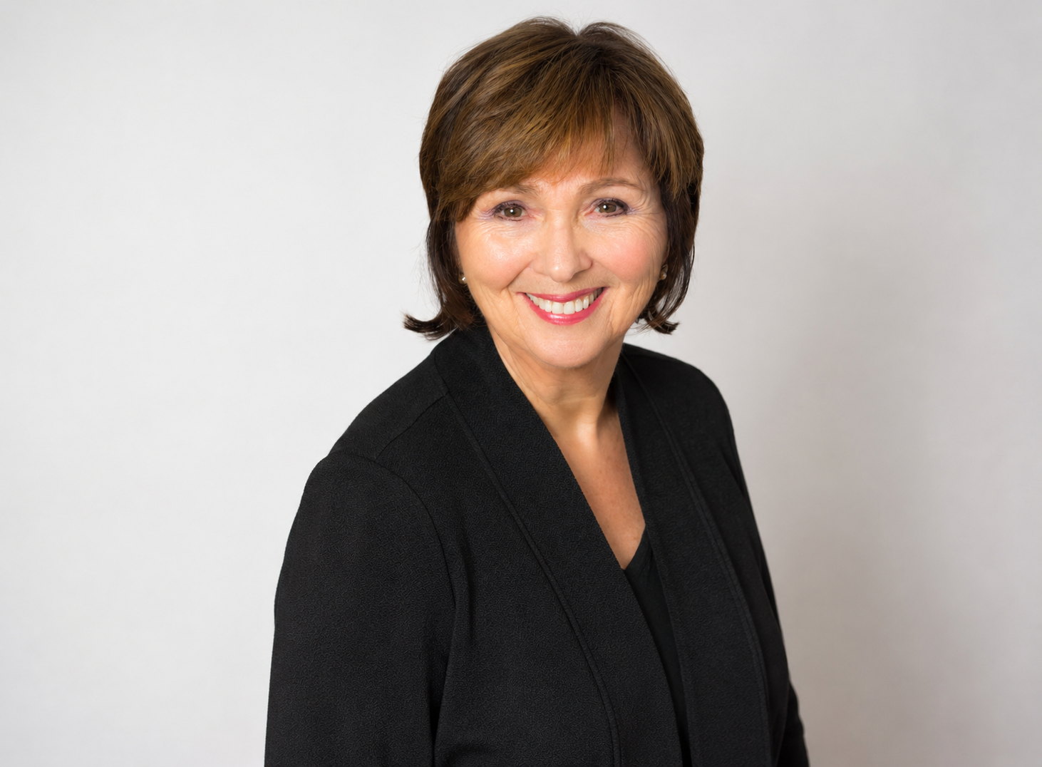 Headshot of a smiling middle-aged woman with short brown hair, wearing a black blazer, against a plain light background.