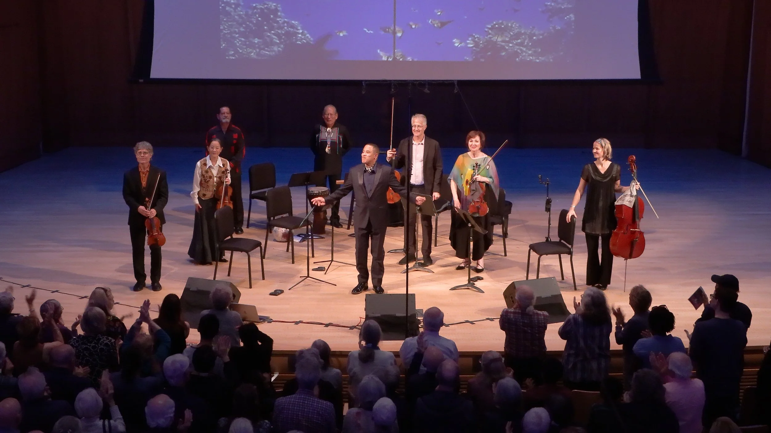 Orchestra on stage with conductor and audience applauding.