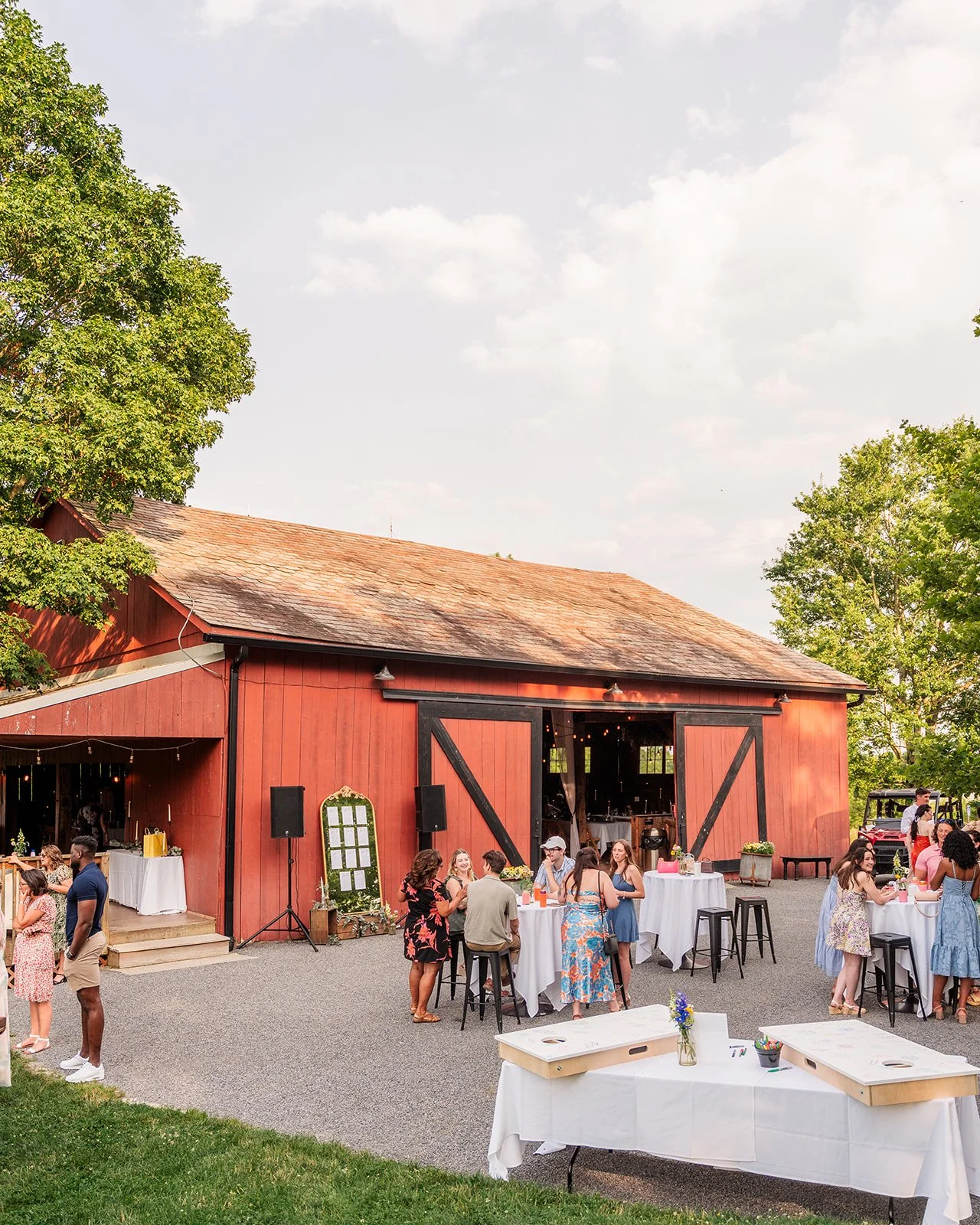 People gathered outside a red barn for a social event, with some chatting around tables, and others standing near a decorated area.