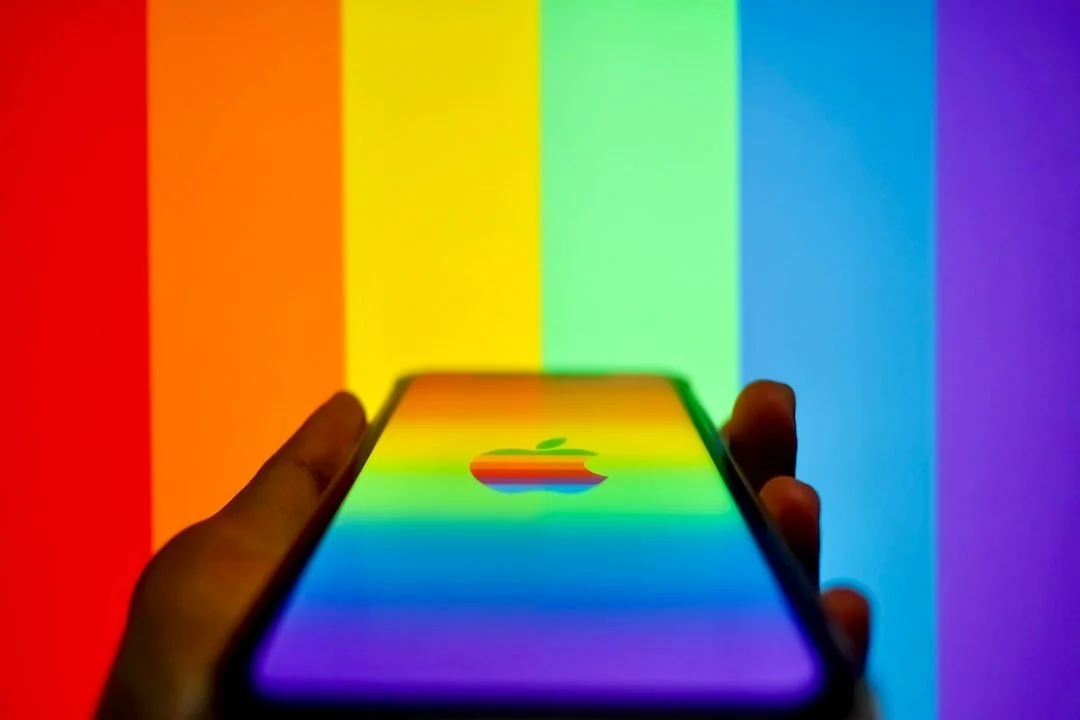 image of hand holding apple phone with rainbow background