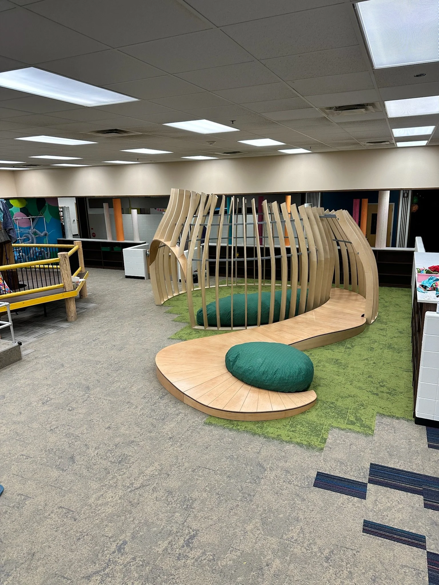 Indoor playground with wooden structure and green cushions in a spacious room.