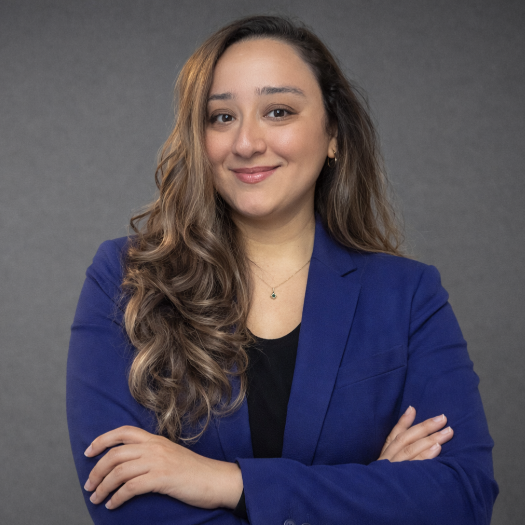 Portrait of a woman in a gray blazer with long hair, wearing hoop earrings and a necklace, inside a circular frame.