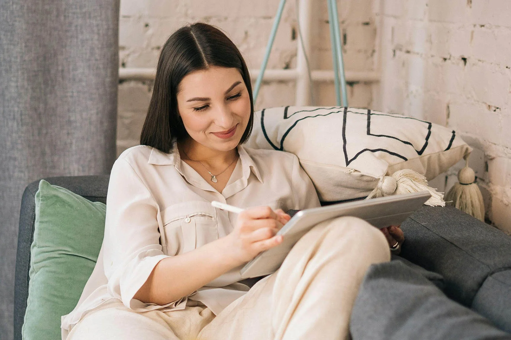 therapist smiling while working on a tablet while sitting on gray couch