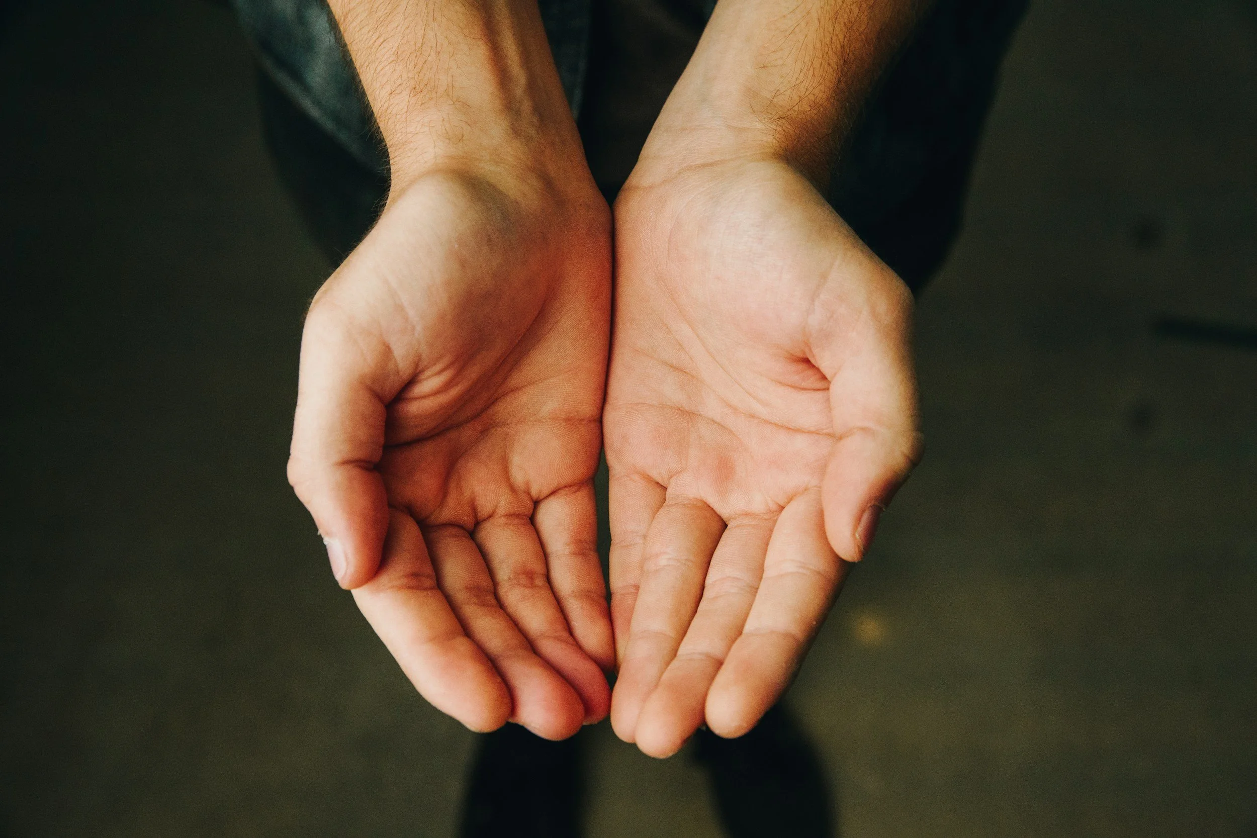 Two open hands held in front, palms facing up, with fingers slightly curled, against a dark background.
