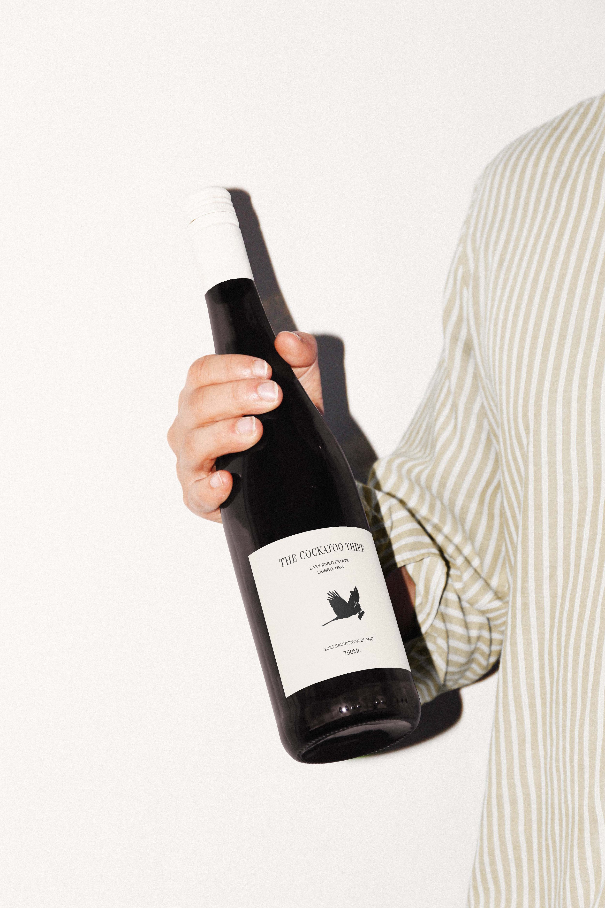 Person holding a bottle of wine with a white label featuring a black bird silhouette.