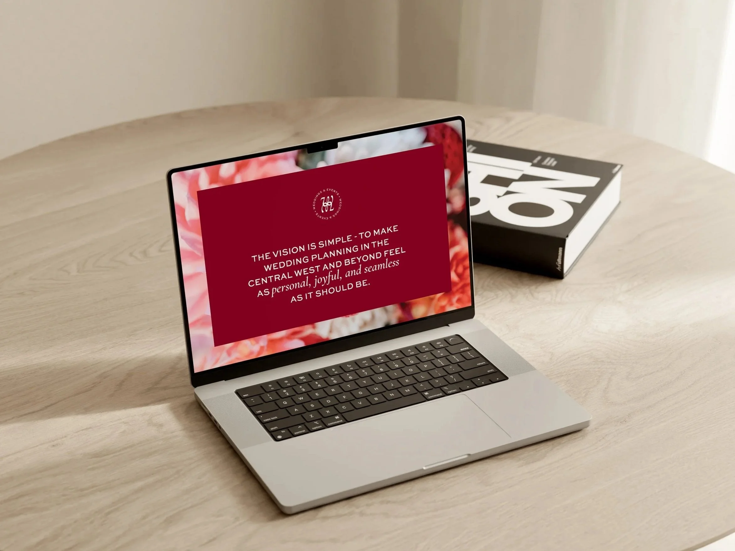 Open laptop on a wooden table displaying a red screen with white text about wedding planning vision, with a closed black and white magazine nearby.