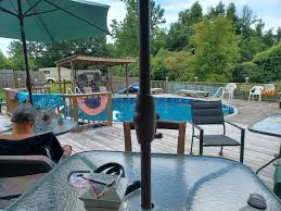 Outdoor patio with a pool, patio furniture, and a child sitting at a table under a large umbrella
