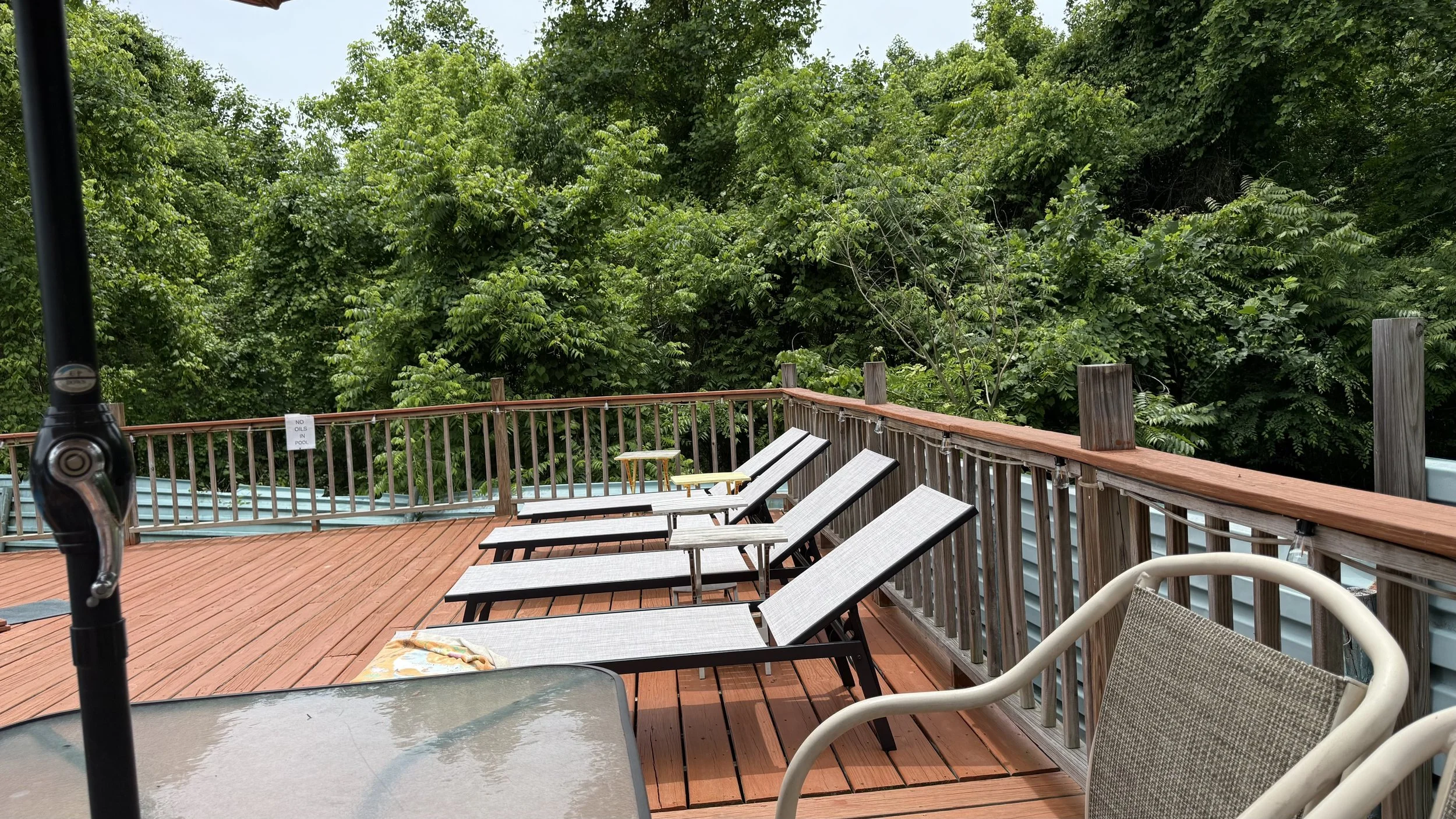 Outdoor wooden deck with lounge chairs and a table, surrounded by trees.