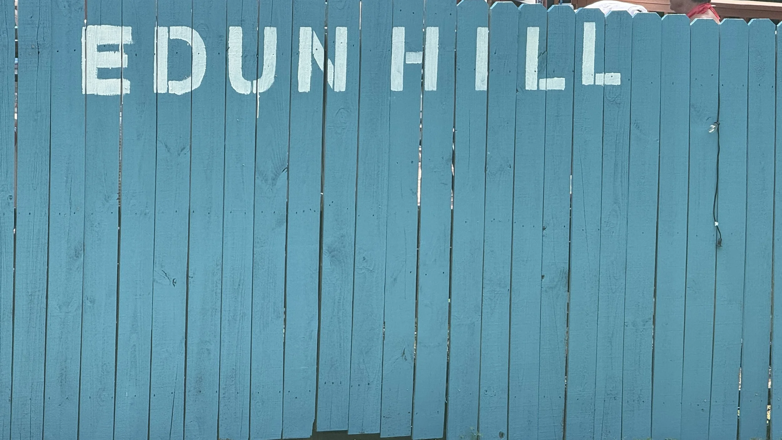 Blue wooden fence with white painted letters spelling 'EDUN HILL'.