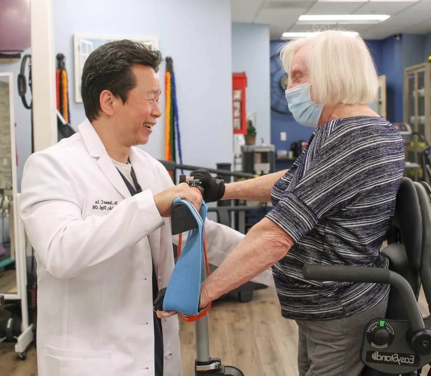 A healthcare professional and an elderly woman with a walker smiling at each other in a rehabilitation center.