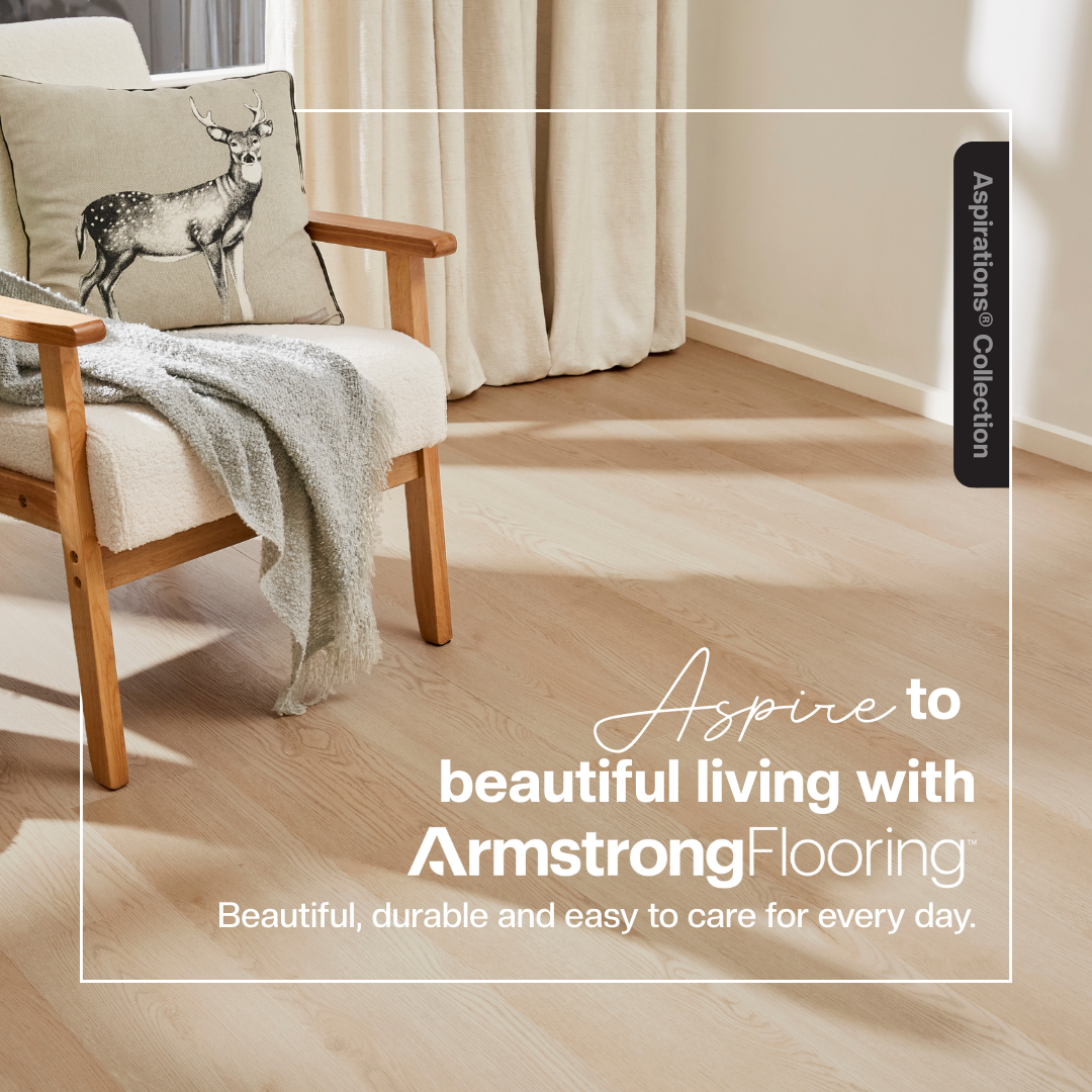 Living room with a beige armchair, a decorative pillow with a deer print, a gray throw blanket, light wood flooring, and neutral curtains.