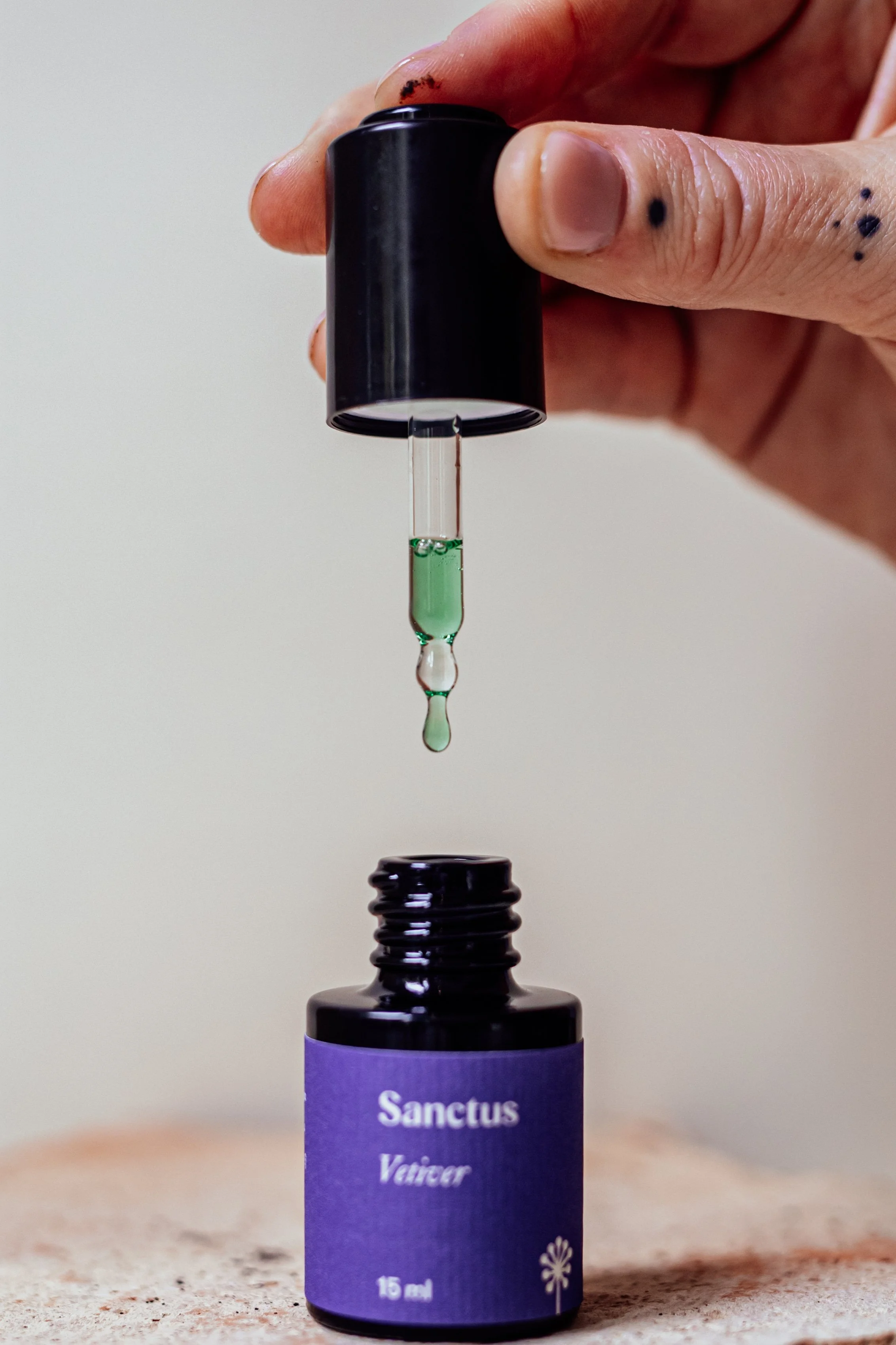 Sanctus Vetiver bottle with dropper releasing emerald-green oil — Vetiveria zizanioides (Khus), hydro-distilled in India.