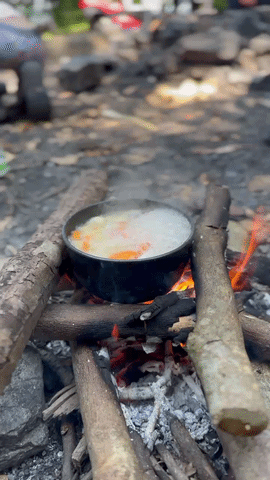 Cooking pot of food simmering over the open campfire the family lit themselves on Pulau Ubin