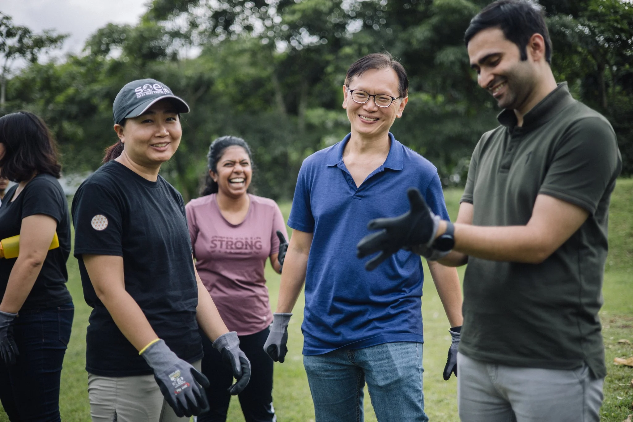 Colleagues in work gloves laughing during a break in a corporate team building programme on Pulau Ubin, Singapore.