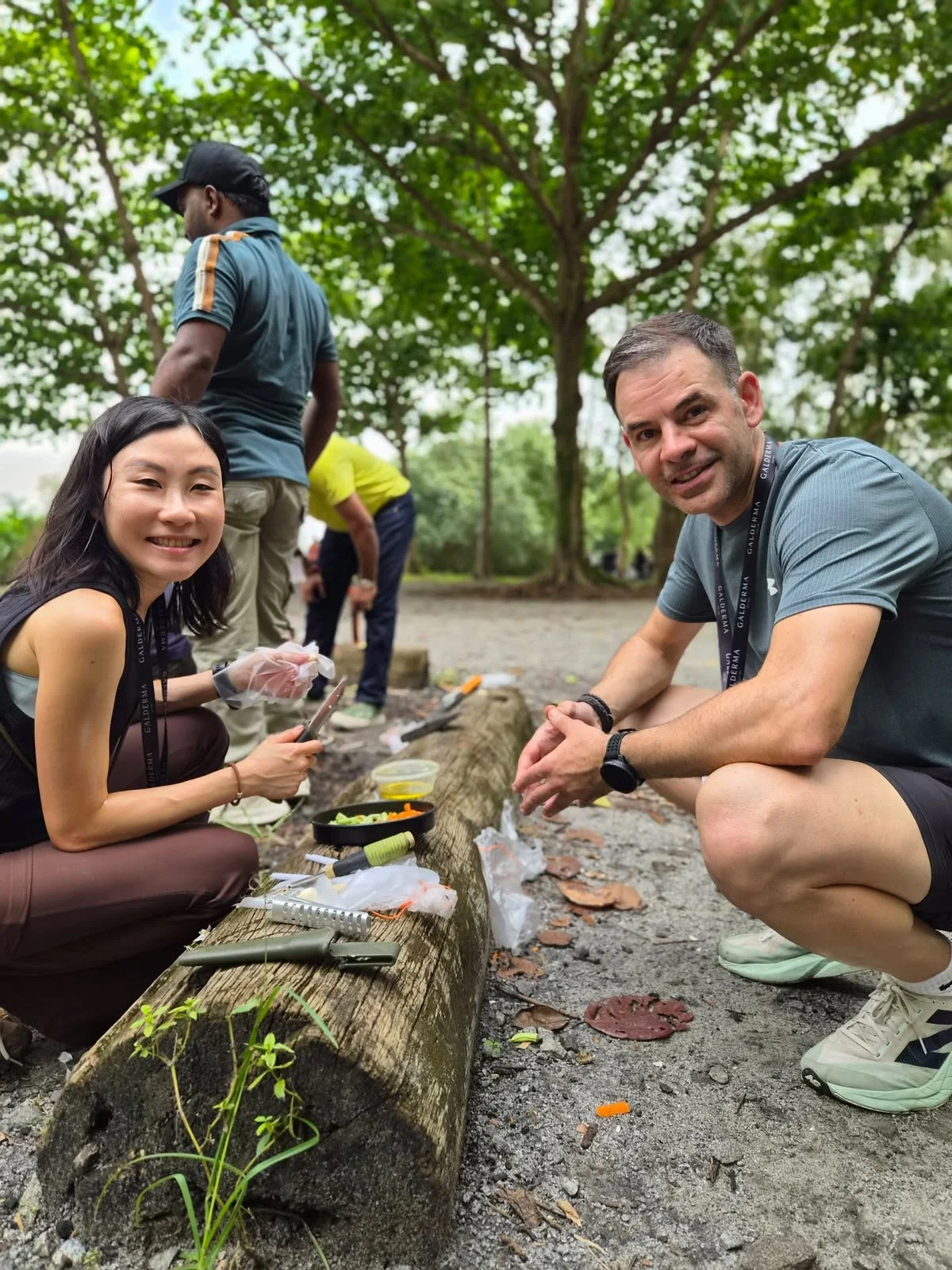 Two colleagues smiling together while cooking at an outdoor team bonding station