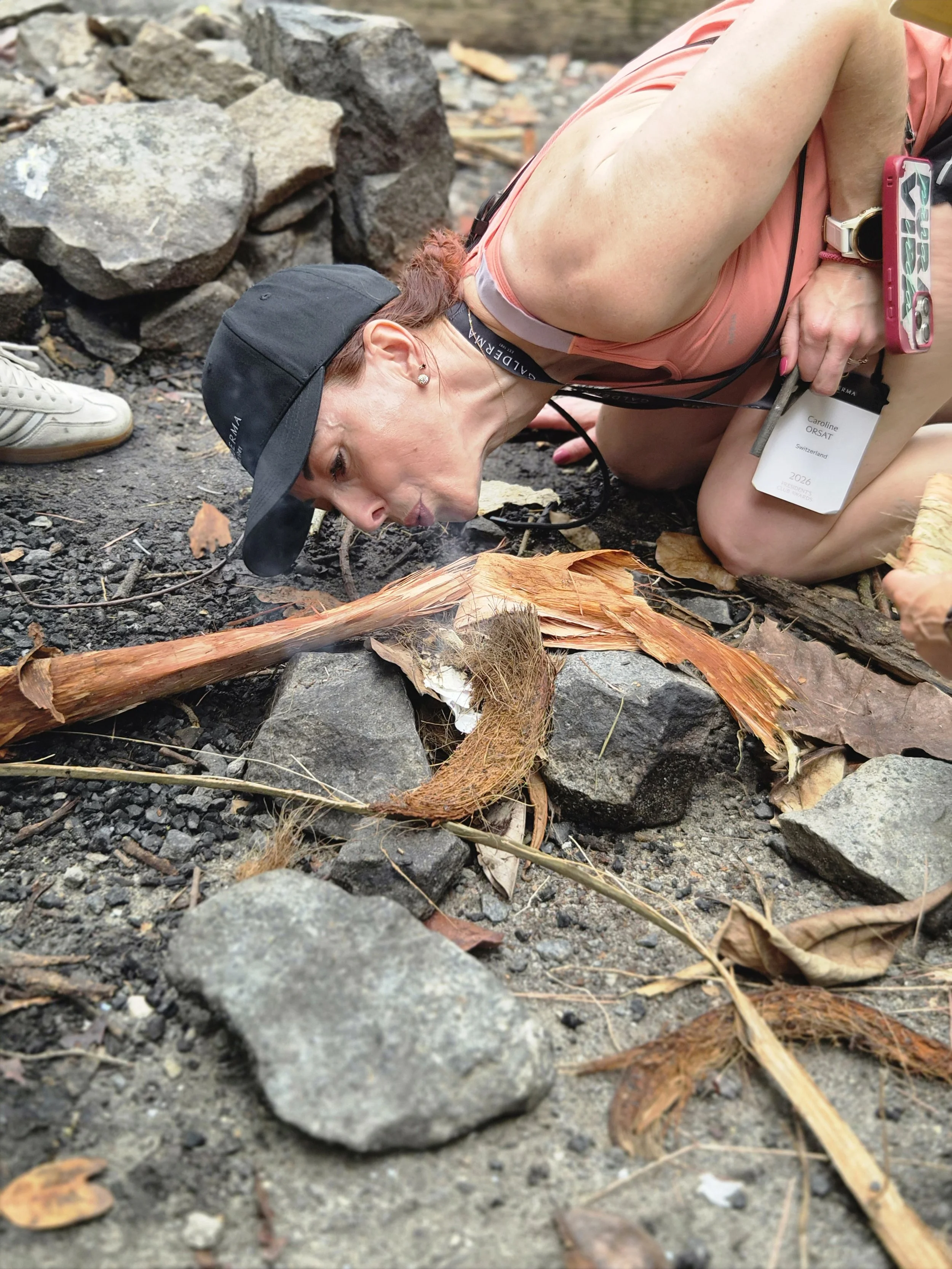 Participant carefully tending a small fire built from natural materials outdoors