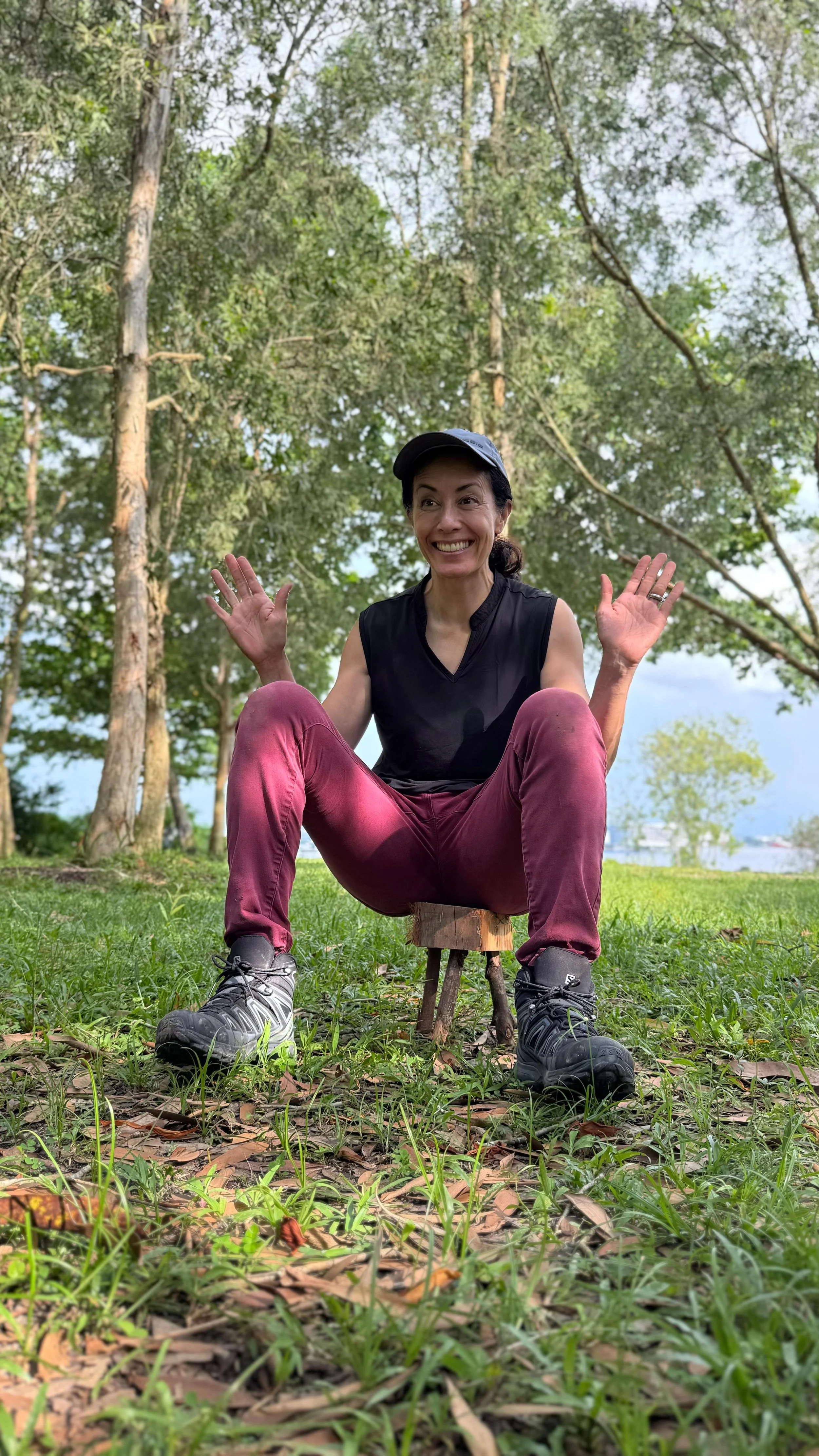 Woman crouching on the grass in a clearing by the water with her arms open