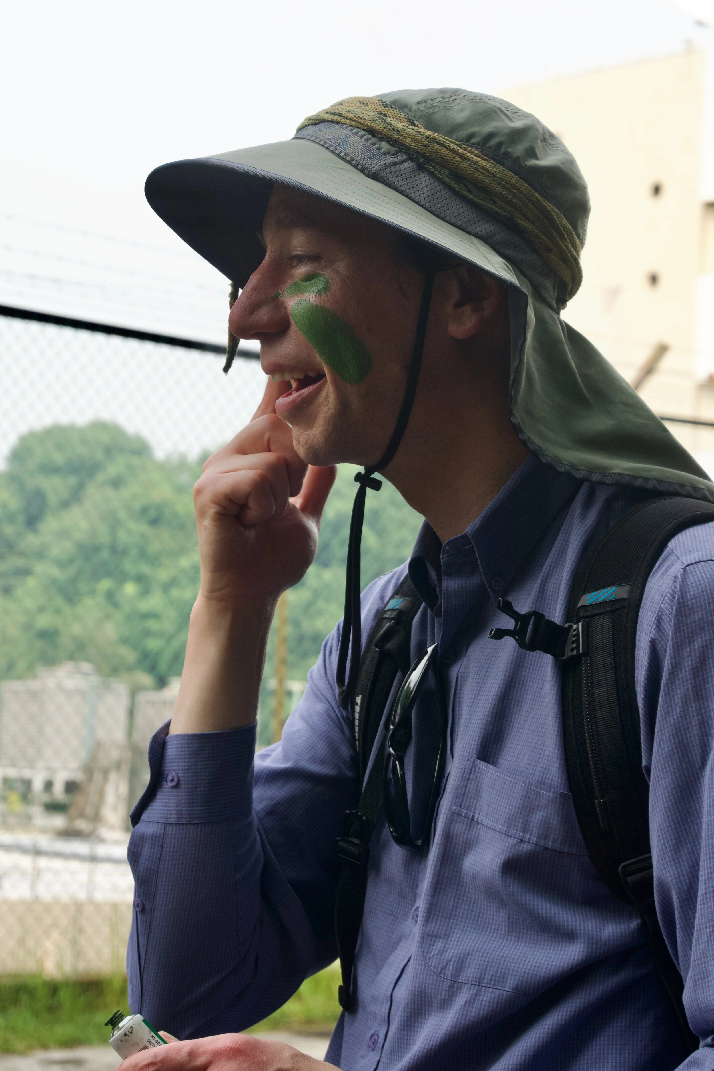 Participant in a bush hat applying green camouflage paint to his face at Fort Serapong