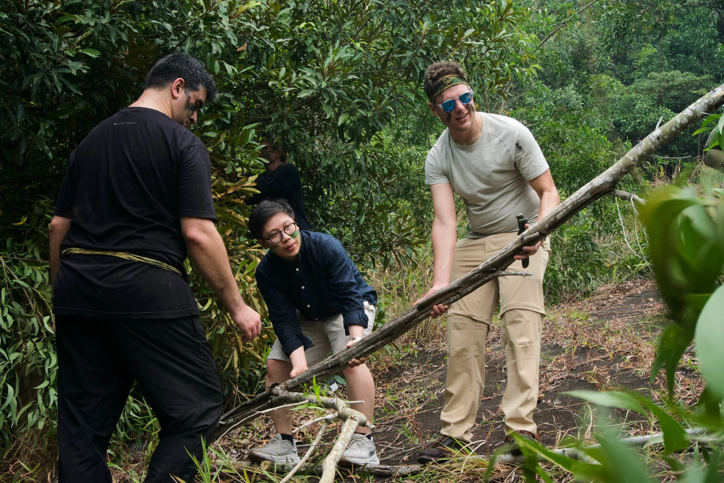 Citadel Securities participants carrying a long branch through vegetation at Granite Hill to build a natural shelter.
