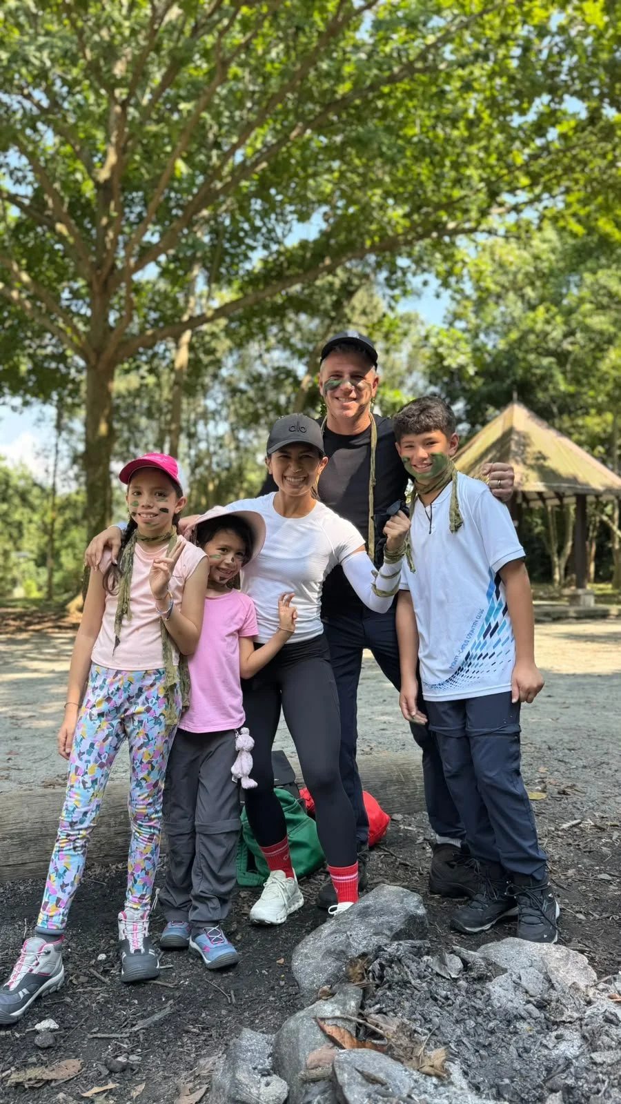 Family of five in camouflage face paint standing together under trees at a private family survival workshop in Singapore